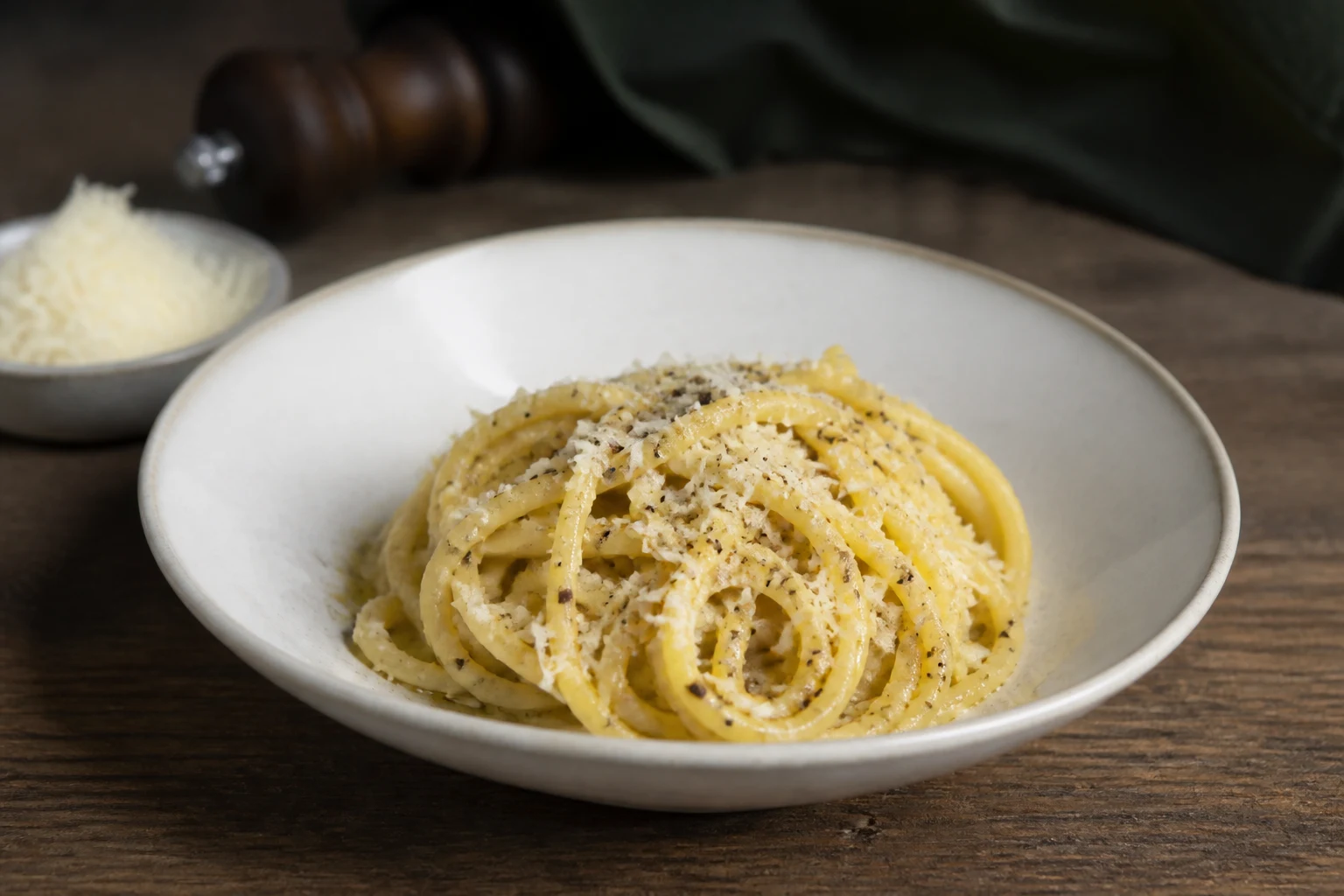 Assiette creuse de pâtes cacio e pepe, pecorino râpé et poivre noir à côté